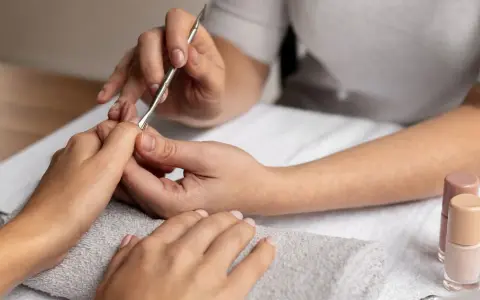Profesjonalny manicure kombinowany w toku. Dłonie są zadbane, a kosmetyczka precyzyjnie pracuje narzędziami.