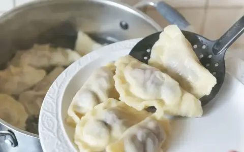 Gotowanie pierogów: gdy wypłyną na powierzchnię, gotuj jeszcze 2-3 minuty. Na talerzu czeka porcja świeżo ugotowanych, parujących pierogów.
