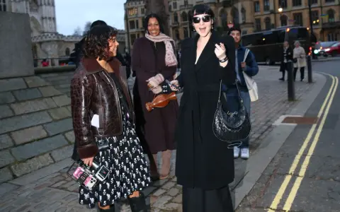 Un elegante cappotto a vestaglia nero, indossato con disinvoltura, si abbina perfettamente a un look audace e moderno.