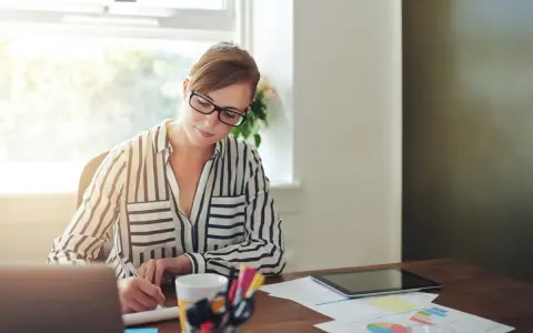 Mujer con gafas trabaja en su escritorio, revisando documentos y gráficos. Quizás está lidiando con gastos de difícil justificación.