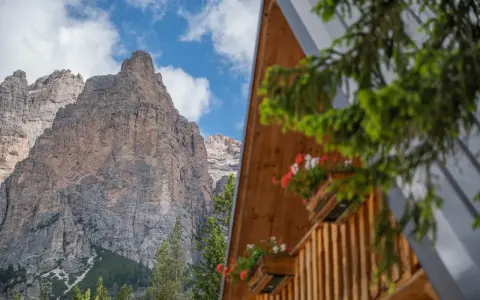 Drewniany domek z kwiatami w skrzynkach na tle skalistych Dolomitów.