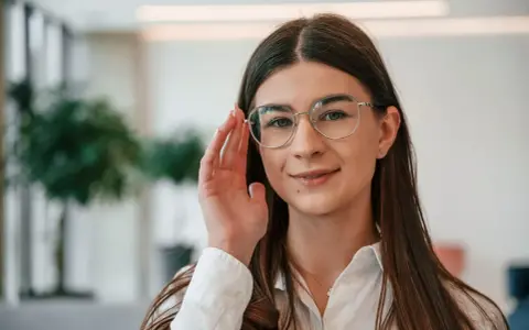Uśmiechnięta kobieta w okularach do czytania i chodzenia poprawia oprawki.