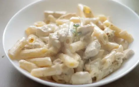 Penne z kremowym sosem i kawałkami kurczaka, udekorowane gałązką ziół. Pyszna potrawka z kurczaka w sam raz na obiad.