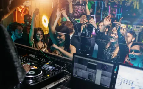 Feiernde Menschen tanzen im Club, während ein DJ auflegt. Eine druckbare muttizettel vorlage zum ausdrucken wäre hier perfekt für die nächste Party!