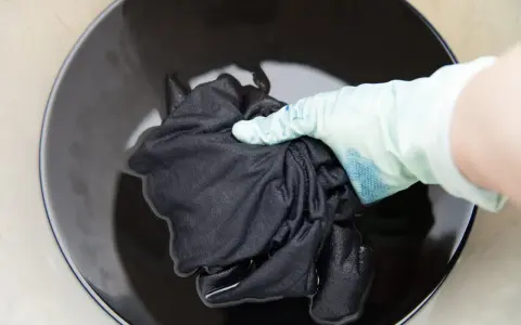 Mano con guante sumerge ropa blanca desteñida de negro en tinte oscuro.