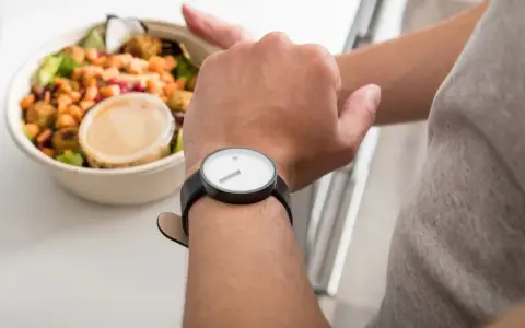 Mann schaut auf seine Uhr, neben einer Schüssel mit Salat. Die Frage: darf man fasten wenn man krank ist?