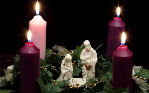 Three lit candles, two purple and one pink, surround a nativity scene. This is the advent 3rd Sunday.