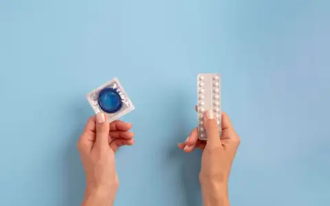 Manos sostienen un preservativo y pastillas anticonceptivas, mostrando opciones de planificación familiar.
