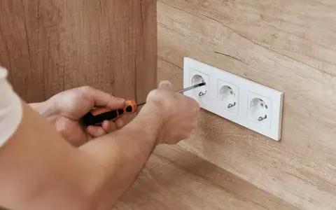 Ręce majsterkowicza przykręcają gniazdko. Dbałość o detale zapewnia bezpieczne napięcie skuteczne w domu.