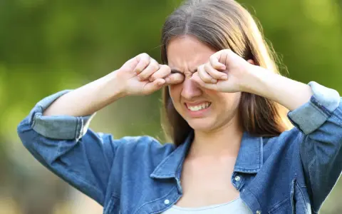 Ragazza con espressione infastidita, si stropiccia gli occhi con le mani, forse per il sole o per la stanchezza.