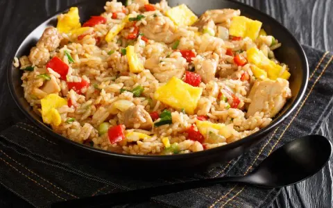 Un plato humeante de arroz chaufa con trozos de pollo, huevo revuelto, pimientos rojos y cebolla verde.