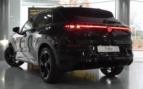 El Volkswagen T-Roc 2026 negro brillante, con sus luces traseras LED rojas encendidas, se exhibe en un concesionario.