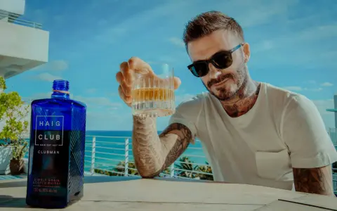 David Beckham z kieliszkiem Haig Club whisky, na tle błękitnego nieba i morza. Idealny moment na relaks.