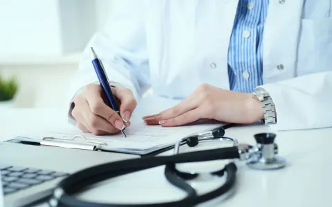Lekarz analizuje wyniki badań, decydując, kiedy zwiększyć dawkę Euthyroxu. Na biurku stetoskop i laptop.