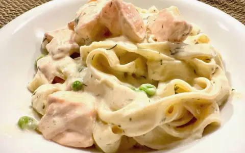 Cremige Nudeln mit Lachs, Erbsen und Dill in einer weißen Schüssel.