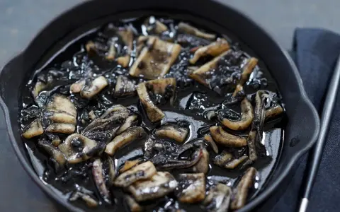 Calamares en su tinta, un plato oscuro y sabroso, servido en una sartén de hierro fundido.