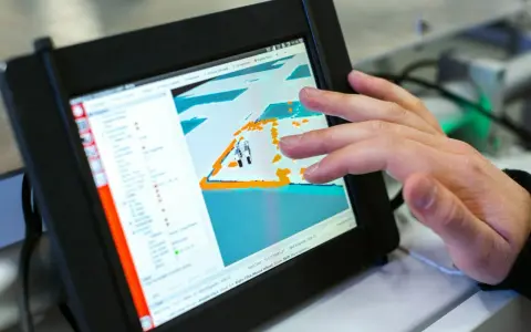 Ein Finger tippt auf ein Tablet, das eine 3D-Ansicht mit einem Roboter zeigt. Die dji app windows wird zur Steuerung genutzt.