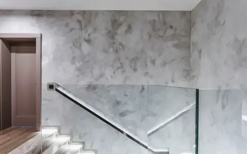 Nowoczesny hol z podświetlanymi schodami i szklaną balustradą. Efektowny tynk na ścianie dodaje wnętrzu elegancji.