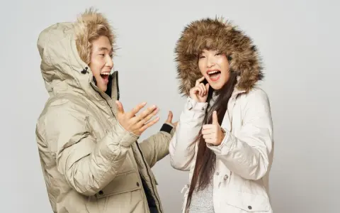 Pareja feliz con abrigos de invierno, ¡el mejor abrigo para el frío! Ella da pulgar arriba, él gesticula.