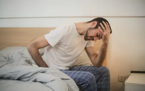 Man med handen mot pannan i sängen, ser ut att ha ont i magen. Hoppas det är något bra mot magsjuka som hjälper snart.