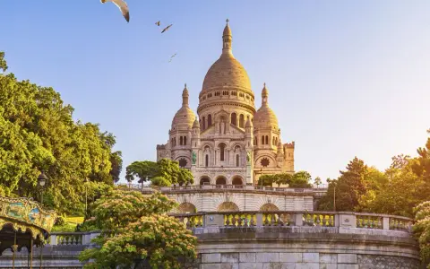 El barrio Montmartre, con la basílica del Sacré-Cœur al fondo, un carrusel y árboles frondosos bajo un cielo azul.