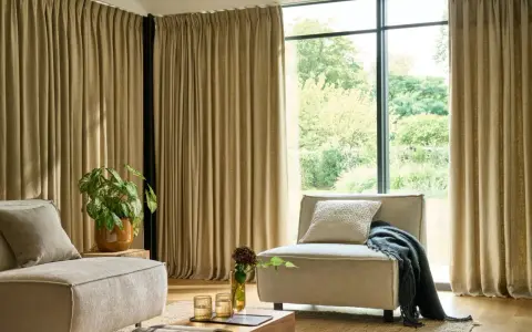 Salon moderne avec canapé beige, fauteuil, plante verte et rideaux au **type de pli rideau** qui habillent une grande baie vitrée.