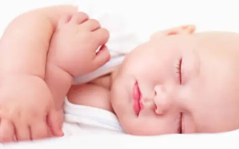 Ein friedlich schlafendes Baby, etwa 4 Monate alt, mit geschlossenen Augen und leicht geöffneten Lippen. Die zarte Haut und die kleinen Händchen sind gut zu erkennen.