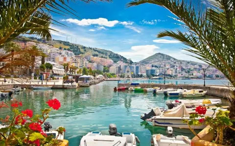 Piękne albania widoki: port z łodziami, palmy i kolorowe miasto na wzgórzu pod błękitnym niebem.