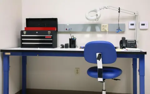 Warsztat z niebieskim stołem, na którym stoi skrzynka z narzędziami, telefon i lampa. Jaka wysokość stołu warsztatowego jest idealna do pracy?