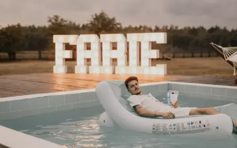 Relaks przy basenie z drinkiem, wielkie litery "FARTE" w tle. Idealny pomysł, jak zorganizować wieczór kawalerski.