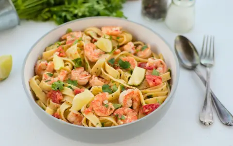 Pyszne tagliatelle z krewetkami, pomidorami i limonką, posypane świeżą natką pietruszki. Idealne danie na szybki obiad.