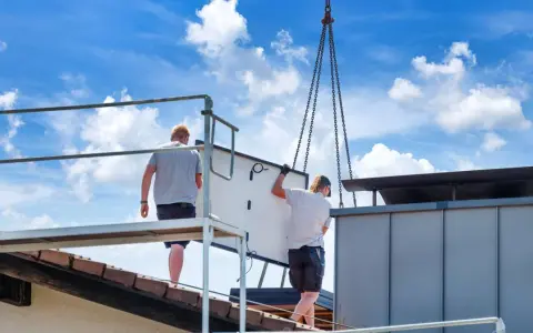 Dwaj pracownicy montują panel fotowoltaiczny na dachu. Ciężka praca i ryzyko wypadku to negatywne skutki fotowoltaiki, które często się pomija.