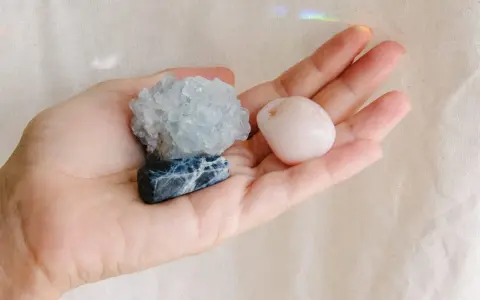 Mano sosteniendo tres piedras: una azul con vetas blancas, una azul pálido cristalina y una rosa pálido pulida. Son piedras para embarazadas.