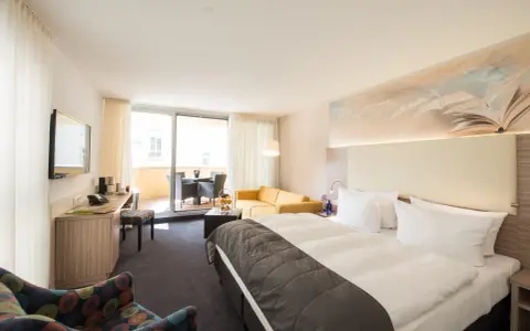 Modernes Hotelzimmer mit Doppelbett, Sofa, Schreibtisch und Balkon.