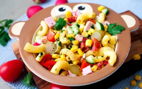 Bunter Nudelsalat mit Mais, Tomaten, Gurken und Schinkenwürfeln in einer Affen-Schüssel – perfekt für Kinder!