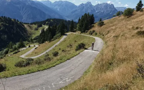 Radfahrer kämpft sich die Serpentinen des Monte Zoncolan hoch. Majestätische Berge im Hintergrund.