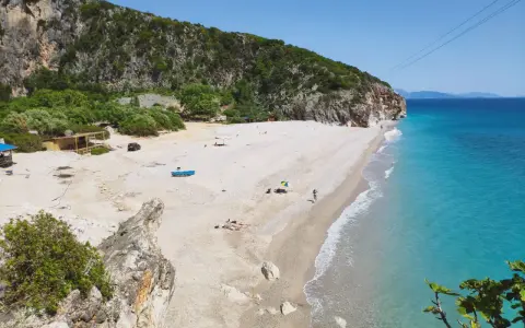 Malownicza plaża Gjipe z turkusową wodą, skalistymi klifami i kilkoma turystami relaksującymi się na piasku.