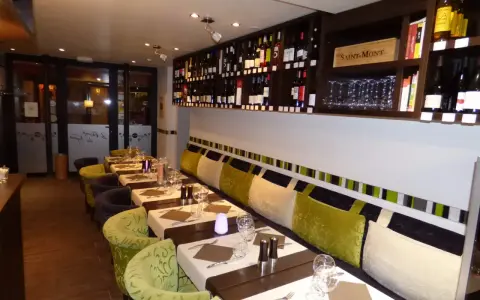 Tables dressées dans un restaurant à Aurillac, idéal pour un repas du dimanche. Les étagères débordent de bouteilles de vin.