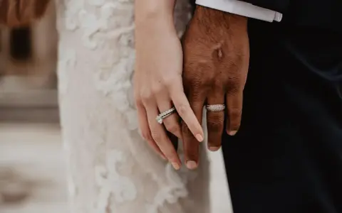 Manos entrelazadas, mostrando el anillo de casada en la mano izquierda de ella y el de él en la derecha.