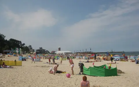 Słoneczna plaża w Darłowie tętni życiem. Ludzie opalają się, bawią z dziećmi i odpoczywają pod kolorowymi parawanami.