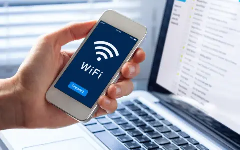 Dłoń trzyma smartfon z ikoną WiFi i napisem "Connect". Obok widać laptopa z listą e-maili, sugerującą pracę zdalną i dostęp do sieci, być może przez **ssid** domowy.