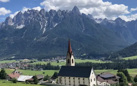 Chiesa con campanile rosso in primo piano, sullo sfondo le maestose vette delle Dolomiti e i **paesi più belli della Val Pusteria**.