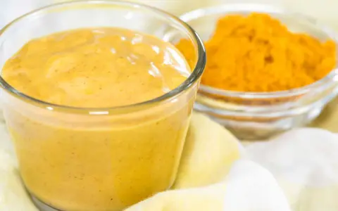 Sauce curry onctueuse dans un verre, avec une coupelle de poudre de curcuma à côté. Parfait pour relever vos plats.