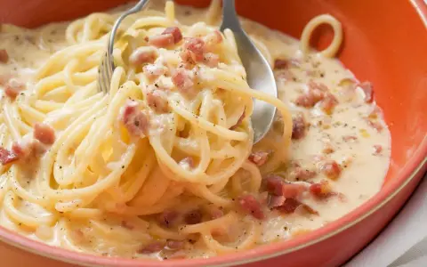 Cremige Pasta mit Ei und Speckwürfeln, ein klassisches italienisches Gericht, serviert in einer orangen Schüssel.