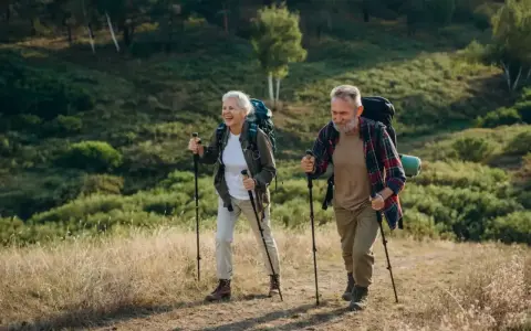 Uśmiechnięta para seniorów z plecakami przemierza leśny szlak, ucząc się, jak chodzić z kijkami.