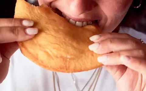 Close-up of a person biting into a golden-brown, fried pastry.