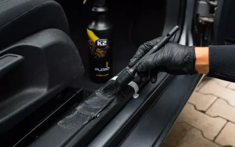 Rękawiczka w ręku z pędzlem K2 Purio detailinguje próg samochodu.