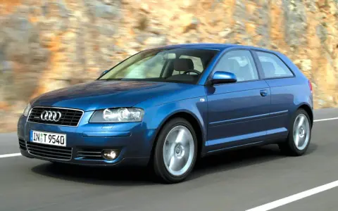 Niebieskie Audi A3 8P w ruchu, z widocznymi przednimi żarówkami, pędzi po drodze wśród skalistych zboczy.