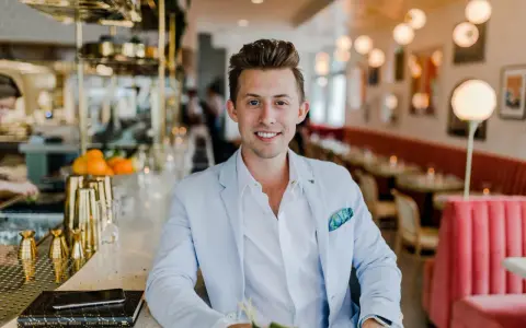 Uśmiechnięty menedżer firmy w jasnoniebieskiej marynarce siedzi przy barze w eleganckiej restauracji.