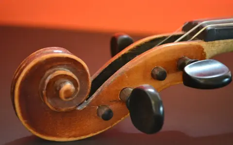 Drewniana ślimacznica skrzypiec, przypominająca spiralę, symbolizuje pierwsze instrumenty muzyczne i ich prostotę.